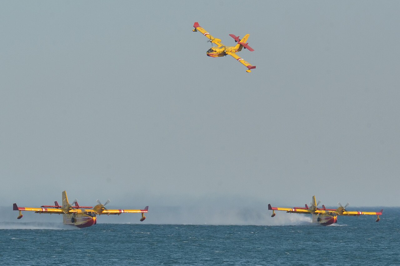 Un Canadair CL-415 rouge et jaune de la Sécurité civile française en vol, train rentré, au-dessus d'un paysage.