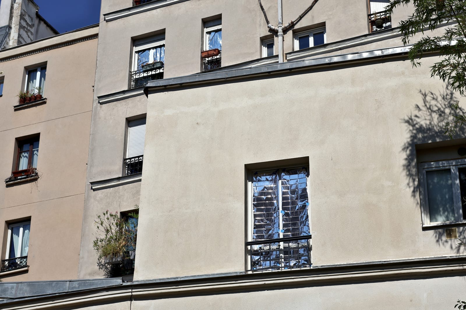 Façade d'immeuble parisien dont une fenêtre est tapissée d'une couverture de survie réfléchissante, rue Henri-Chevreau, en juillet 2026