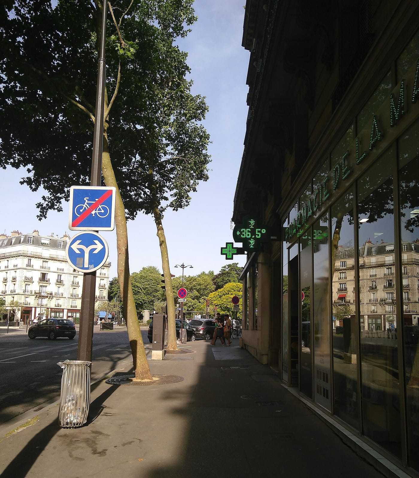 Trottoir parisien ensoleillé pendant une vague de chaleur ; l'enseigne d'une pharmacie affiche 36,5 °C.
