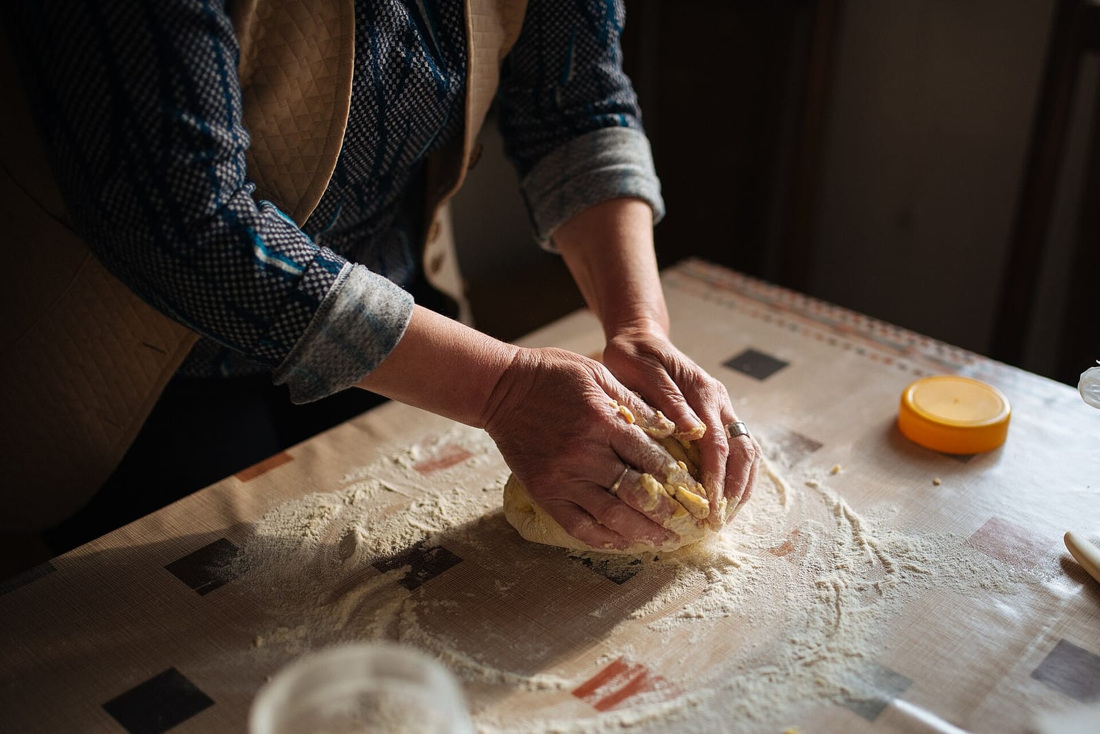 Deux mains pétrissent une boule de pâte farinée sur un plan de travail, les manches relevées.